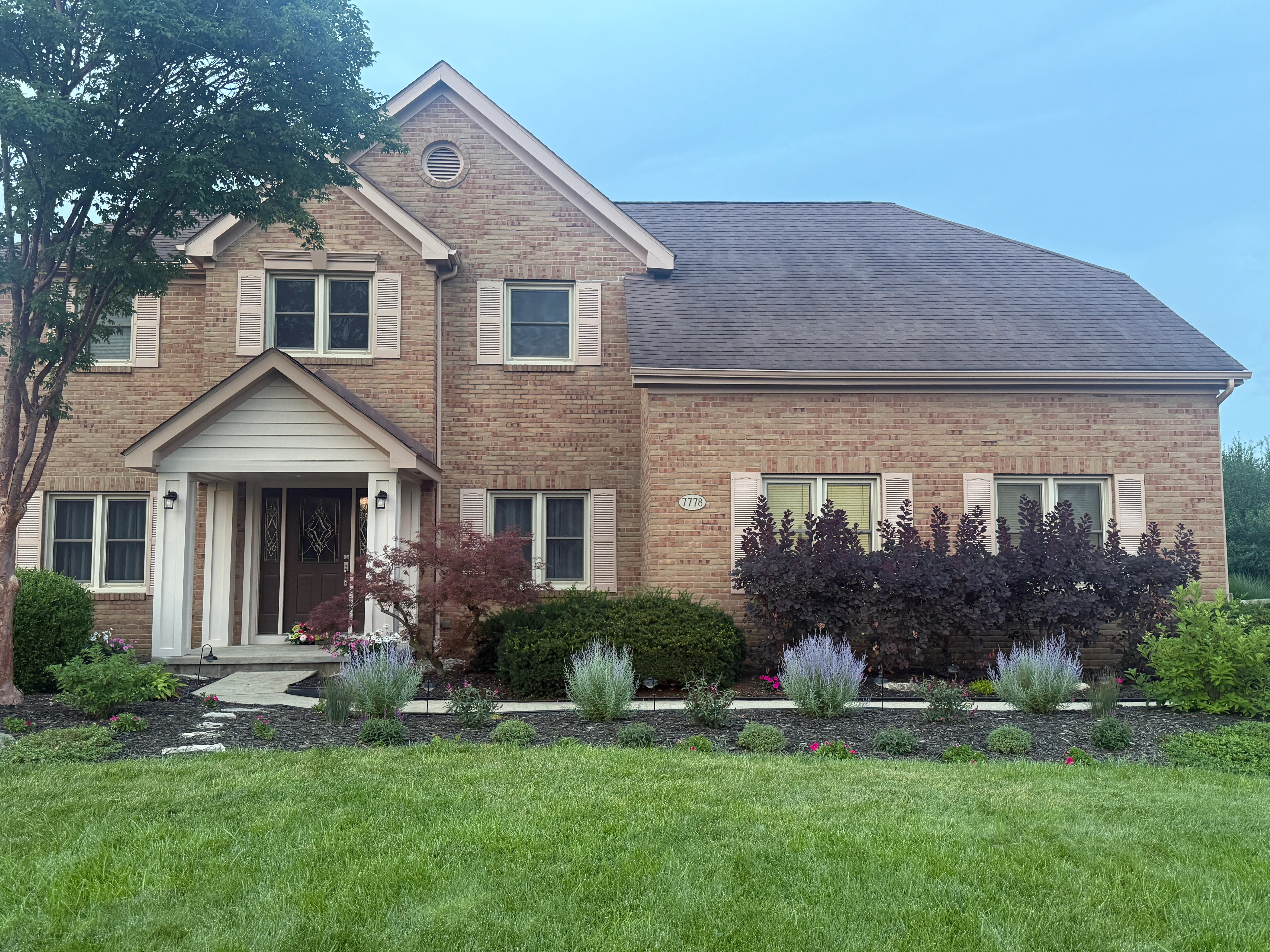 Two-story brick home with white trim, shutters, and landscaped front entrance in New Albany