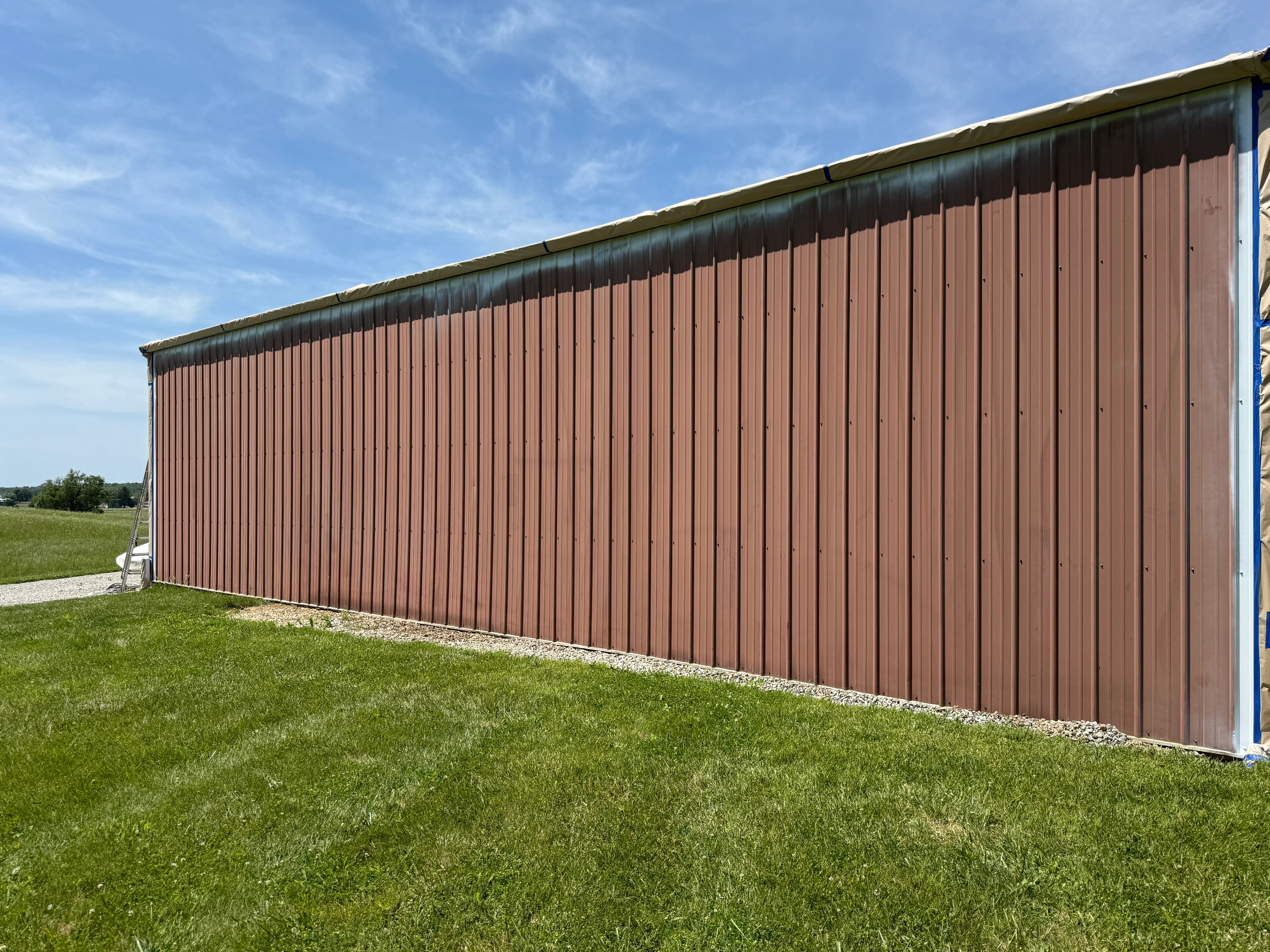 Brown corrugated metal building exterior with painted siding and trim against green lawn