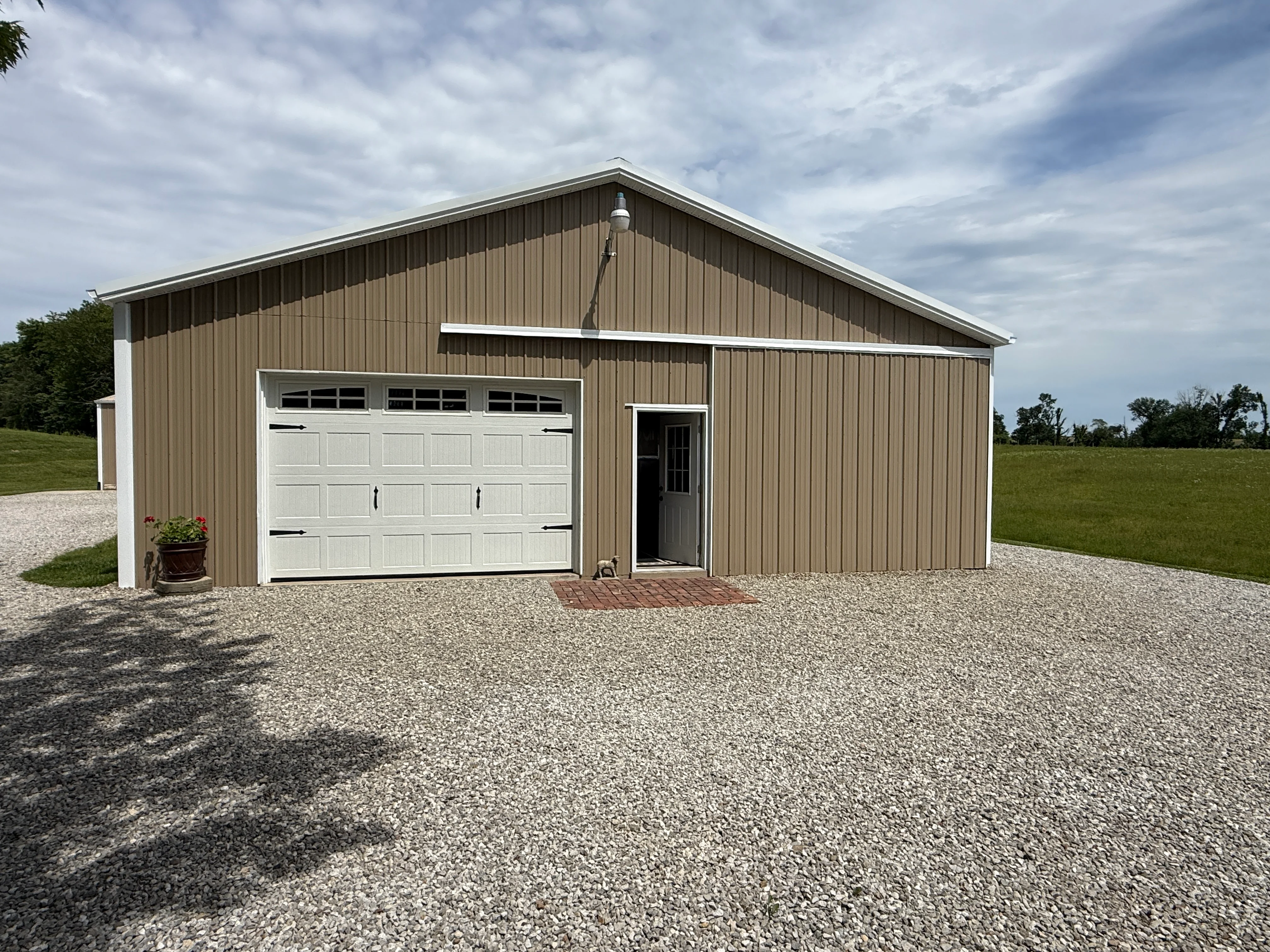 Tan metal garage with white-painted garage door and trim on gravel driveway