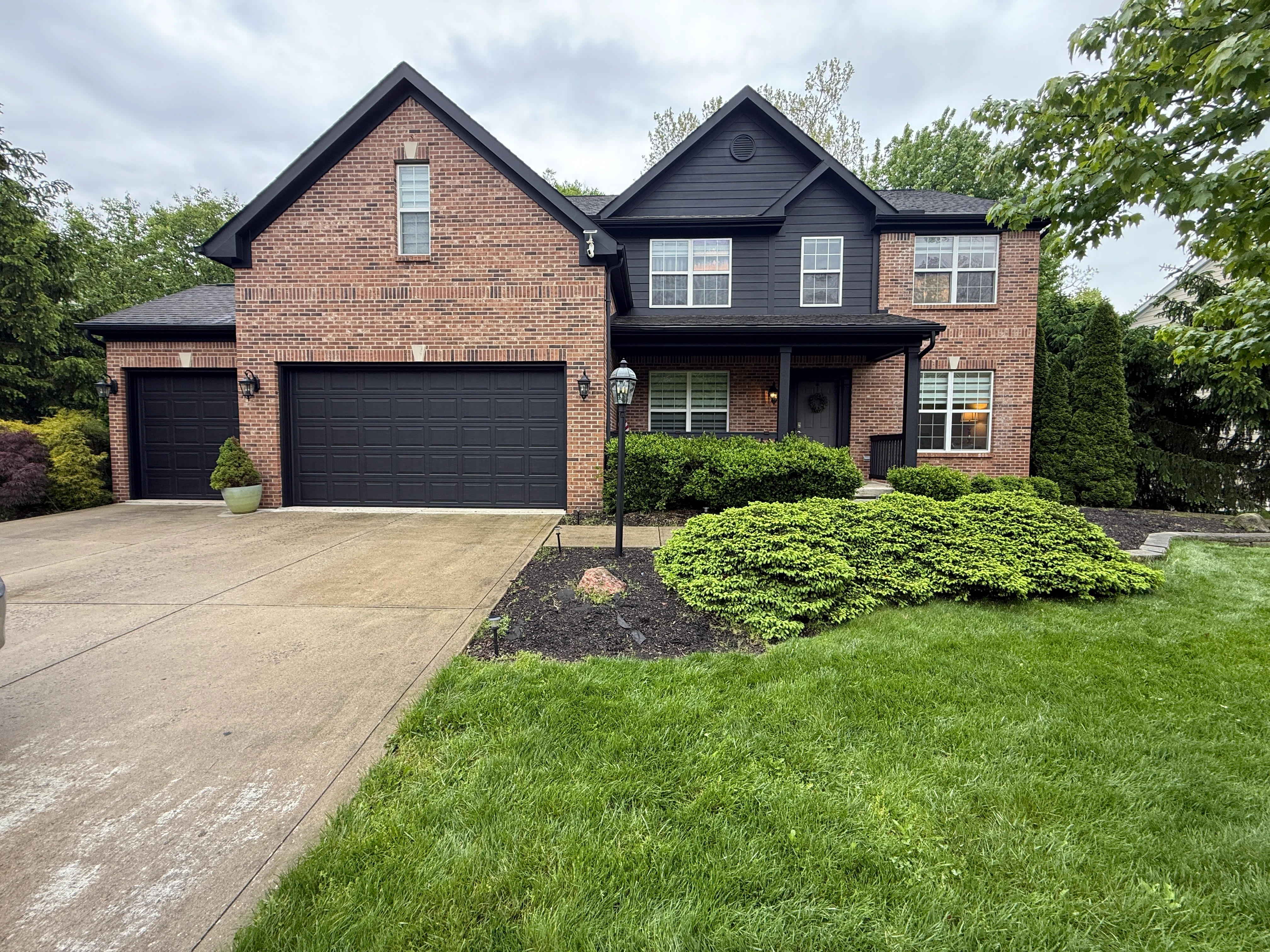 Two-story brick home with black painted garage doors and dark exterior trim in New Albany