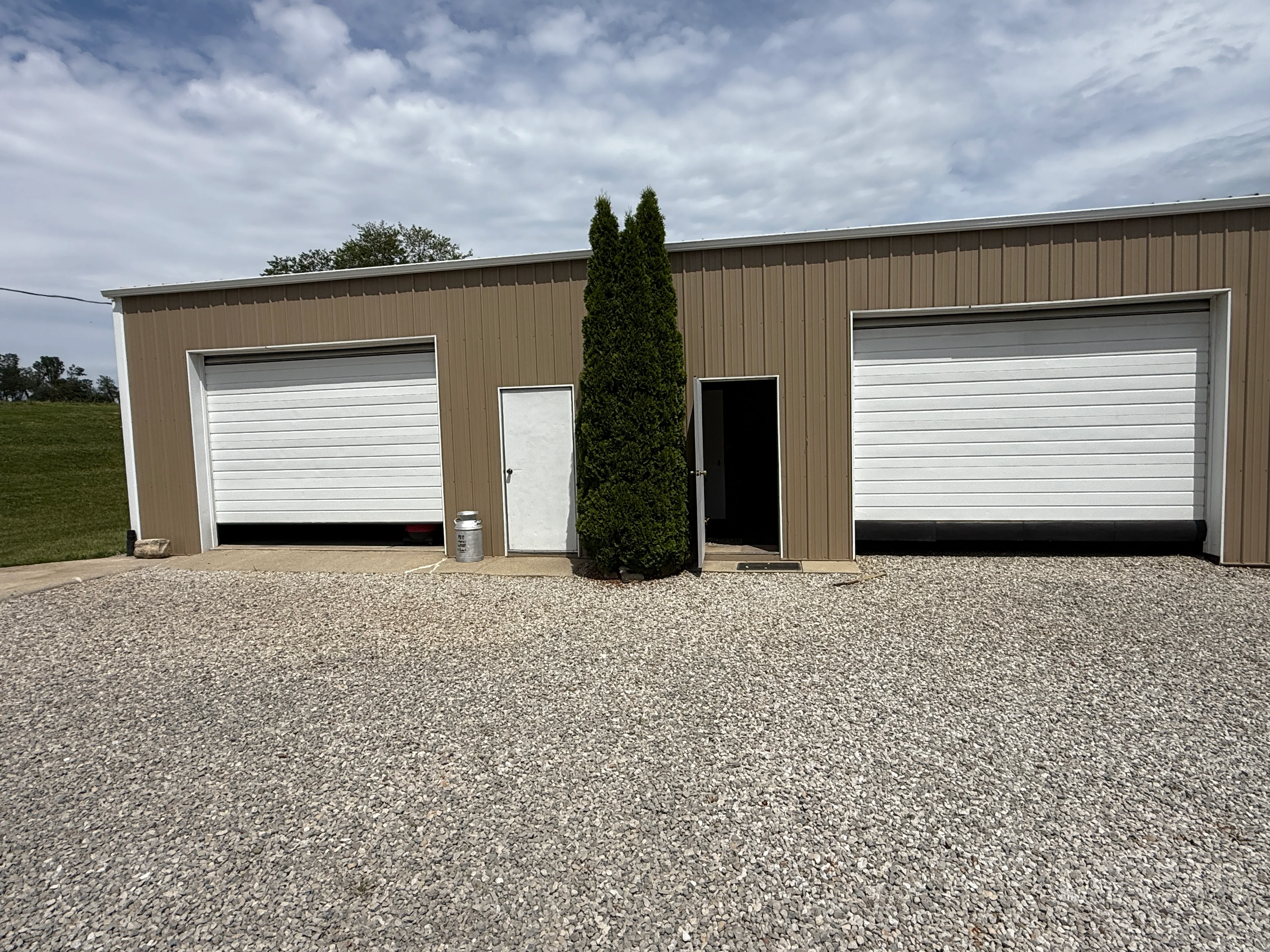 Tan metal garage building with two white overhead doors and white entry door