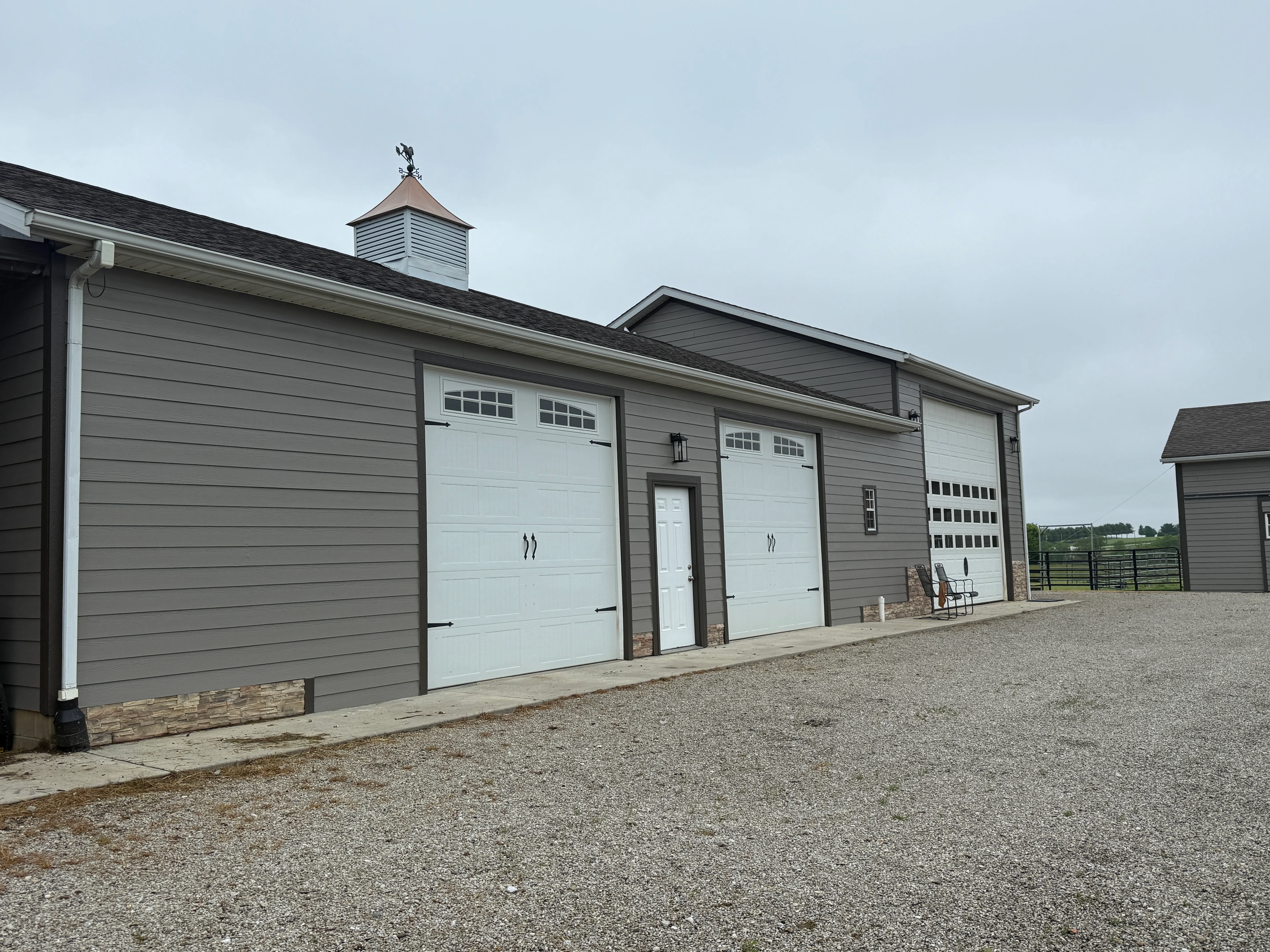 Modern gray barn with white garage doors and stone base accents in rural setting