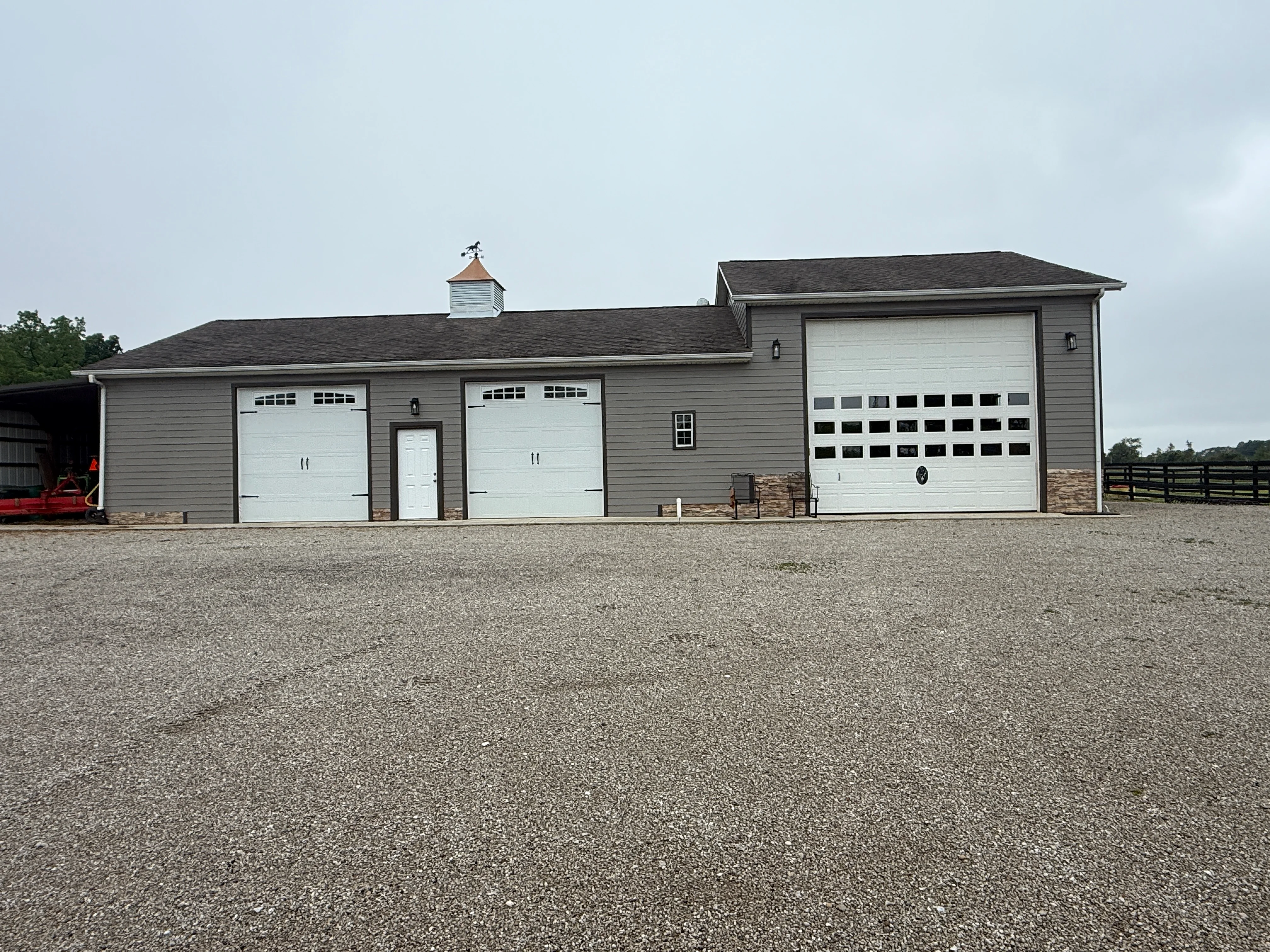 Gray agricultural building with white garage doors and stone foundation accents