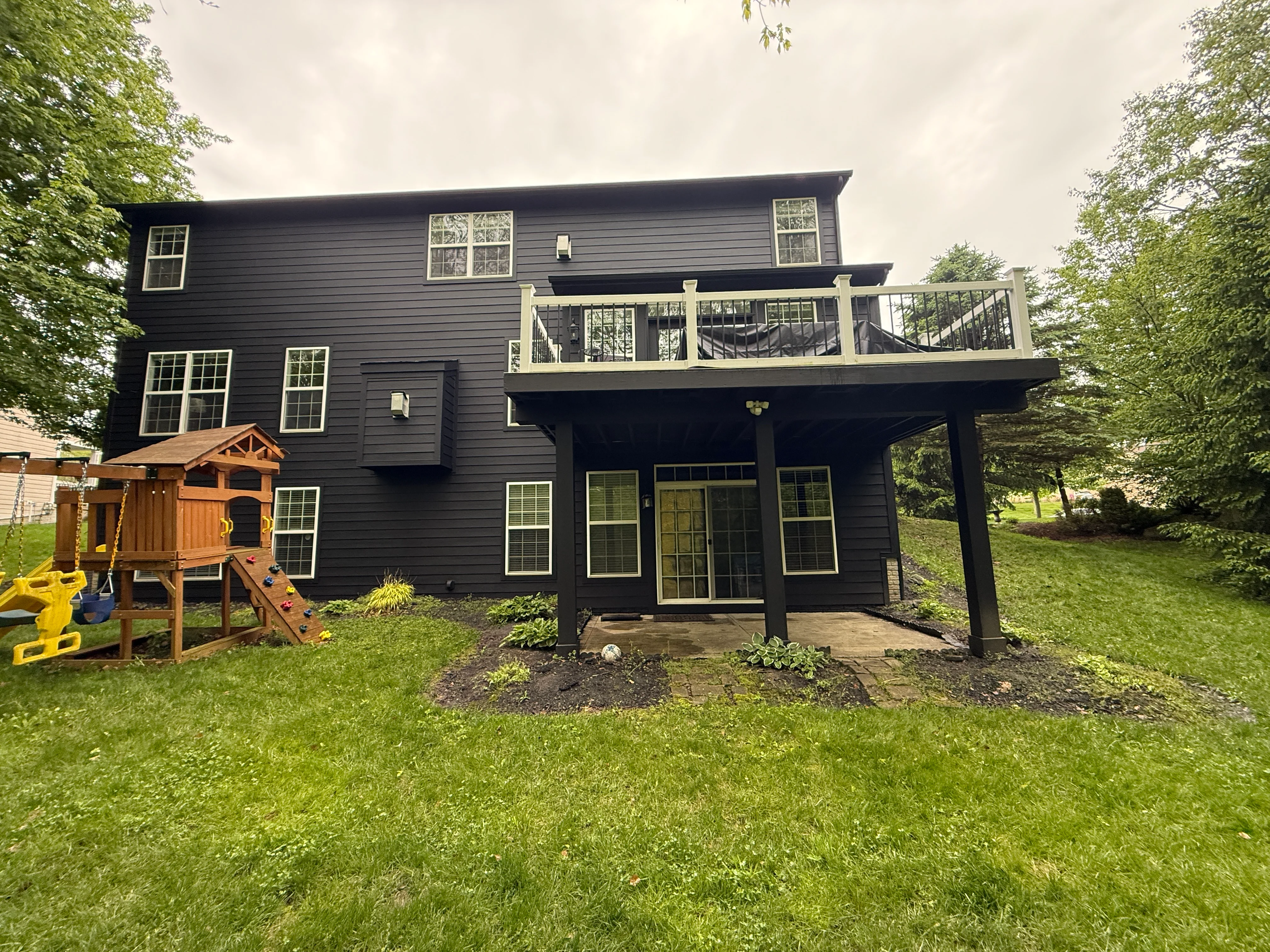 Black painted two-story home with white deck railings and covered patio in New Albany