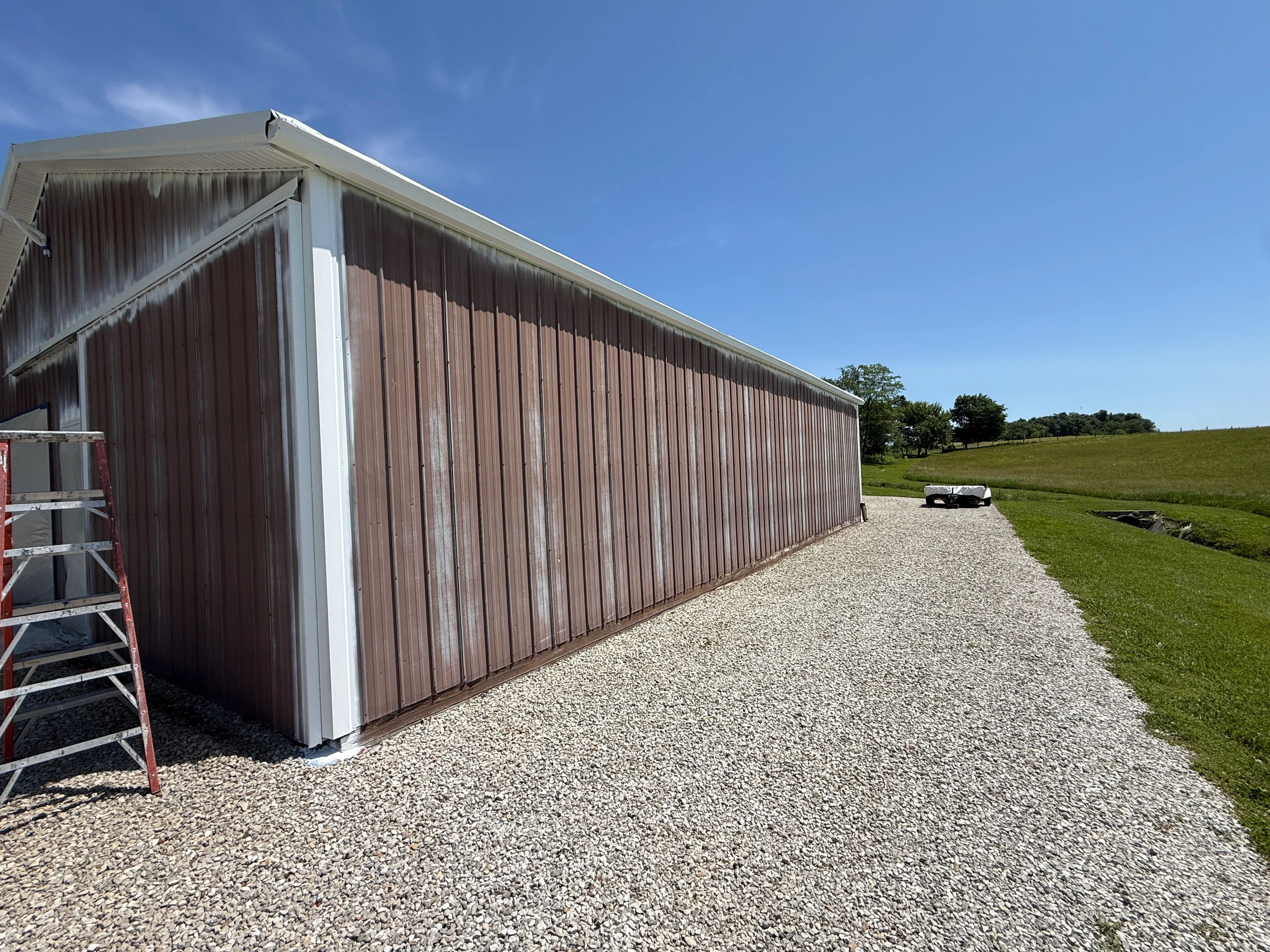 Newly painted agricultural metal building with burgundy siding and white trim on gravel driveway