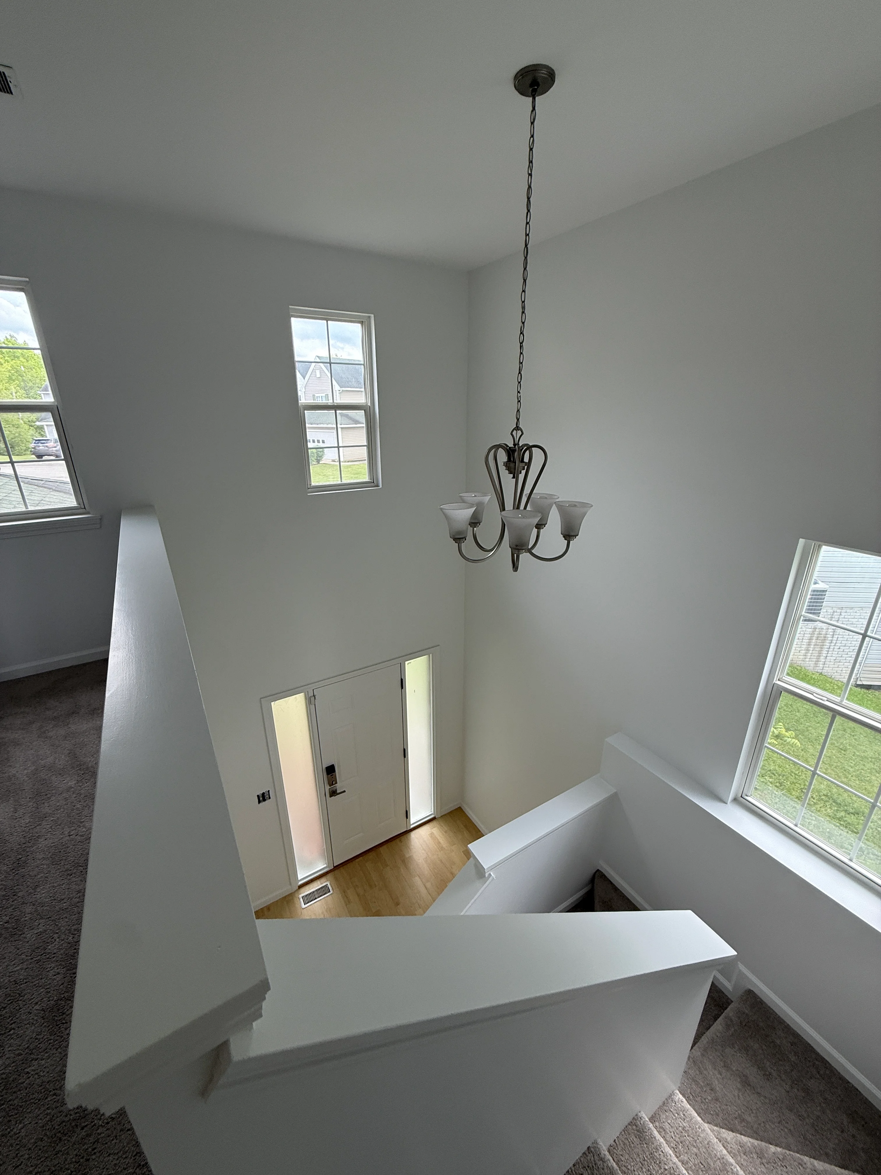 Two-story white foyer with pendant light, windows, and wood flooring