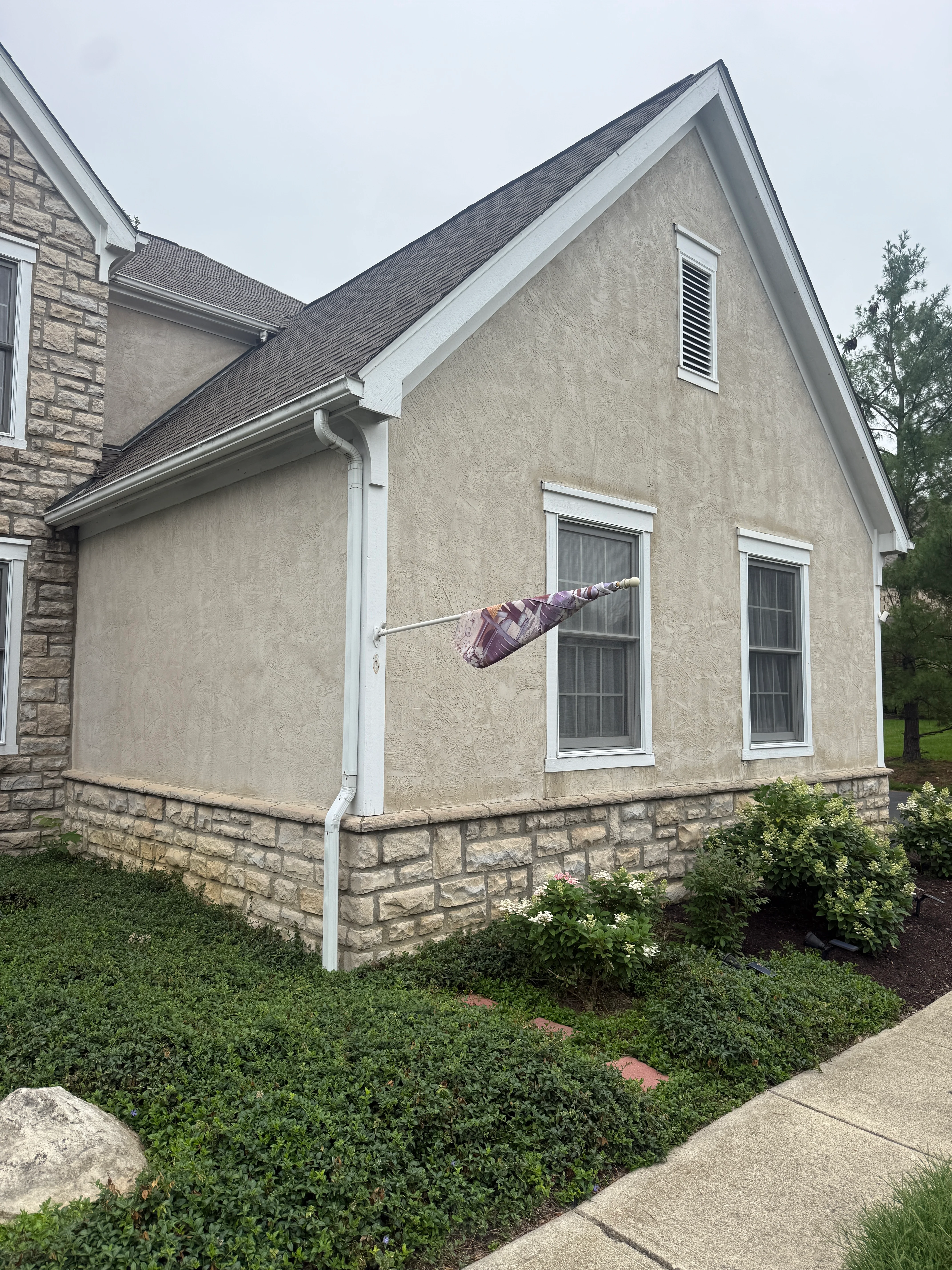 Beige stucco house exterior with white trim, stone foundation, and painted gutters