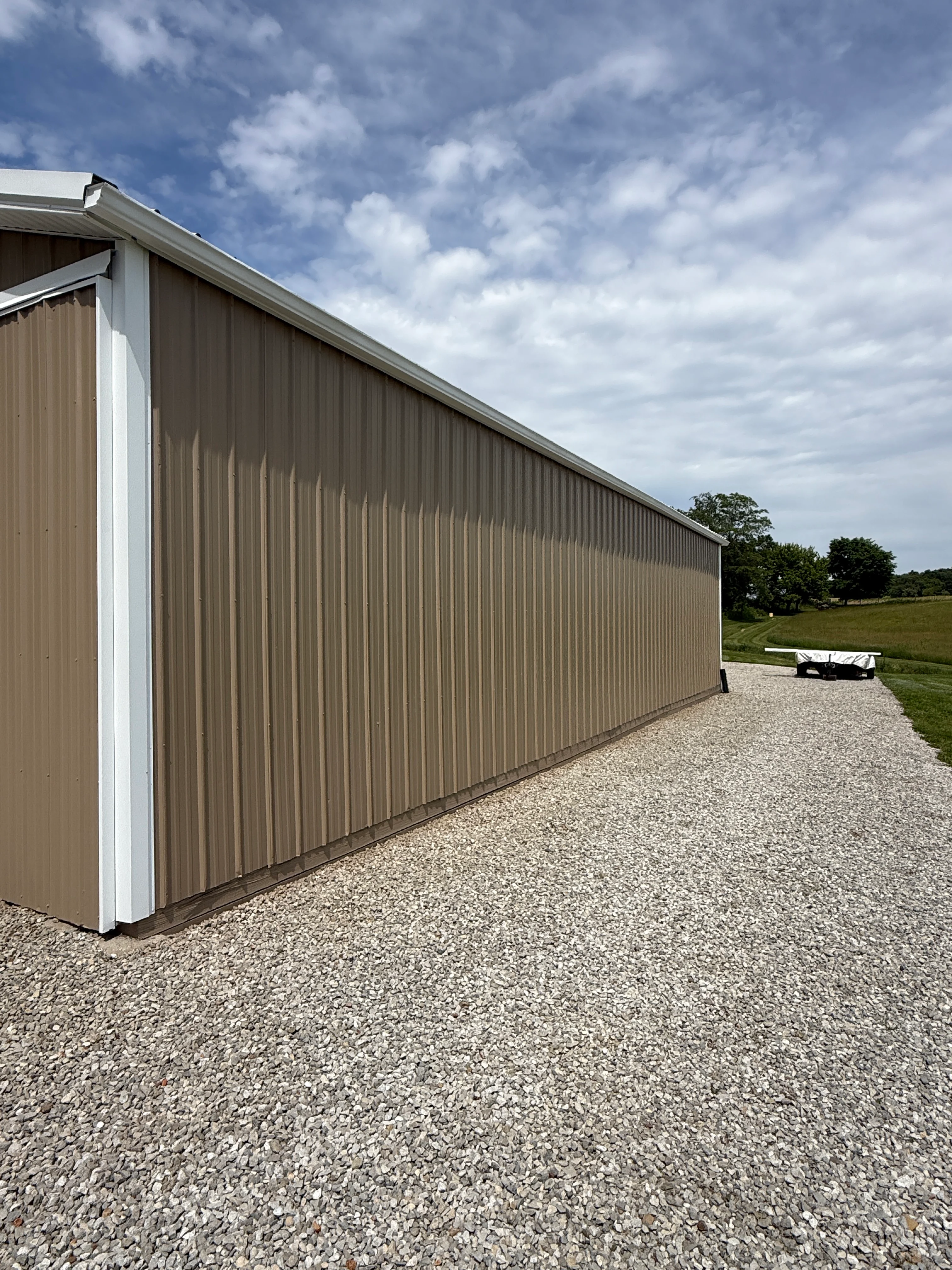 Newly painted metal agricultural building with tan siding and white trim on gravel driveway