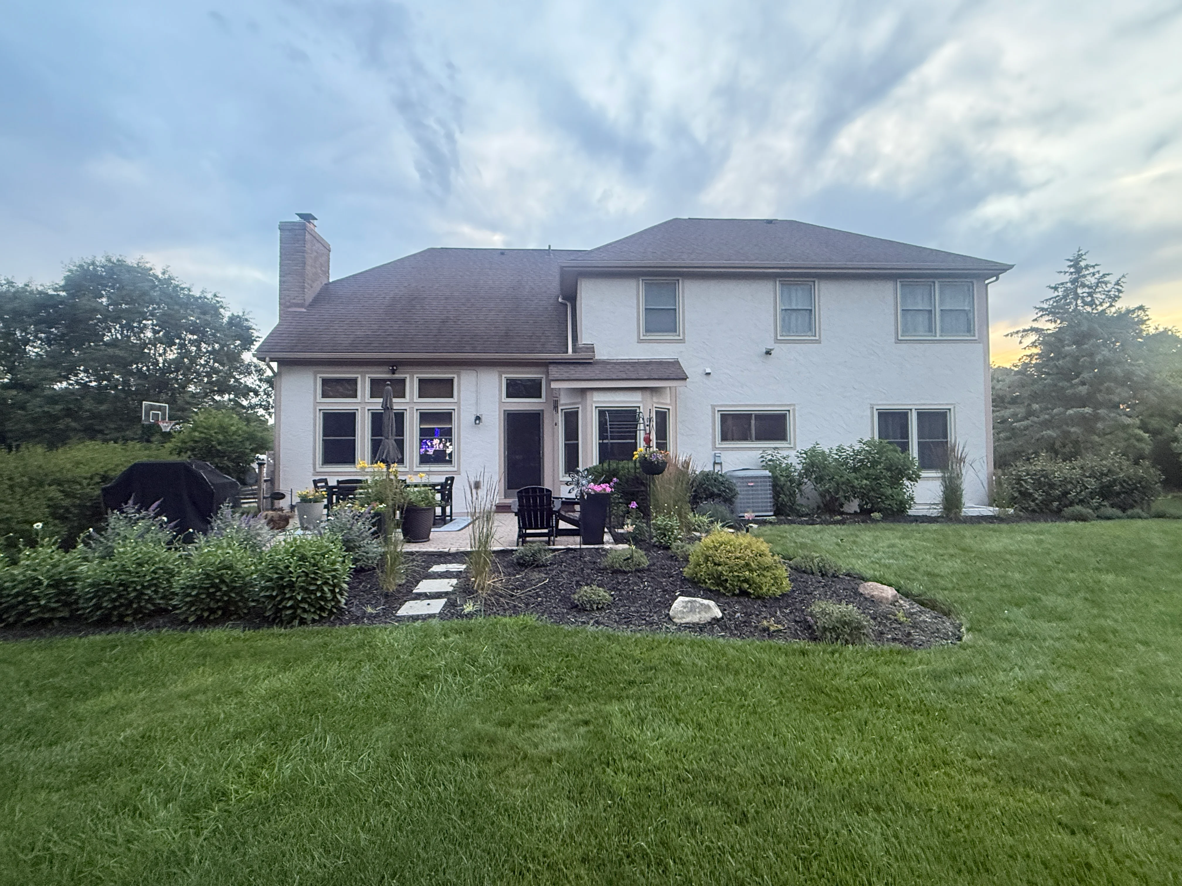 White two-story colonial home with dark roof, brick chimney, and manicured landscaping